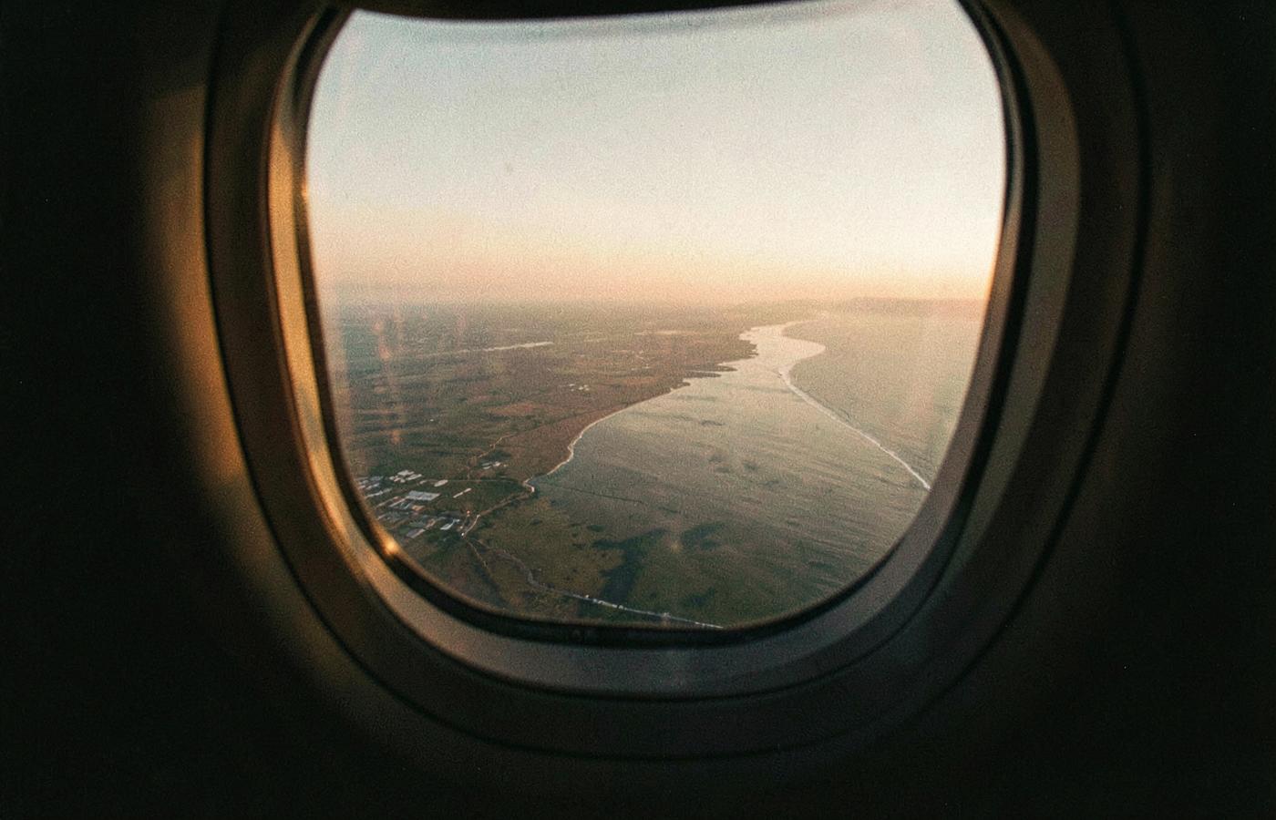 A coastline seen through an airplane window at sunset, the shoreline curving away below — Image accompanying the chapter From Brazil to a New Beginning
